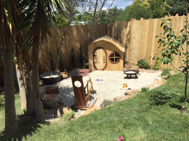Outdoor playhouse set behind a sandpit filled with toys, in the preschool garden